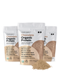 Three bags of Complement Chocolate Organic Protein powder with plant-based ingredients like almond, chia seed, and pumpkin seed. A small pile of the protein powder is in front of the bags.