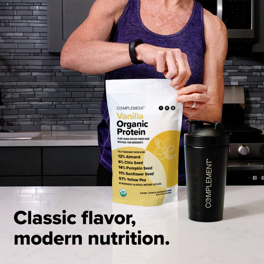 A person in a purple tank top opens a bag of Complement Vanilla Organic Protein beside a black shaker bottle on a kitchen counter. The text reads, Classic flavor, modern nutrition.