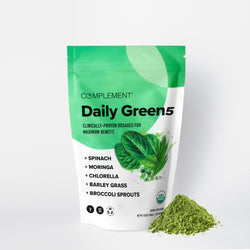 A green and white pouch labeled Complement Daily Green5 stands upright with a pile of green powder beside it. The packaging lists ingredients: spinach, moringa, chlorella, barley grass, and broccoli sprouts.