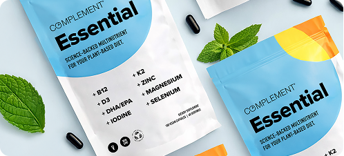 Two blue and white Complement Essential supplement packets are displayed with black capsules, green mint leaves, and an orange packet, highlighting key nutrients like B12, D3, DHA/EPA, iodine, K2, zinc, magnesium, and selenium.