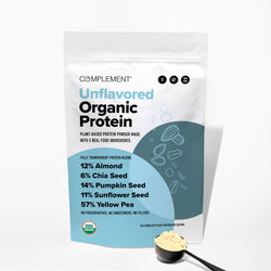 A white bag of Complement Unflavored Organic Protein powder stands upright. The label lists ingredients and percentages, and a black scoop with protein powder lies in front of the bag on a white surface.