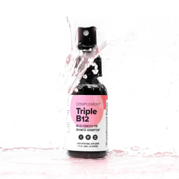 A small dark bottle labeled Complement Triple B12 is splashed with pink liquid. The label mentions Multi-Form B12 for Enhanced Absorption. The background is white, creating a striking contrast.