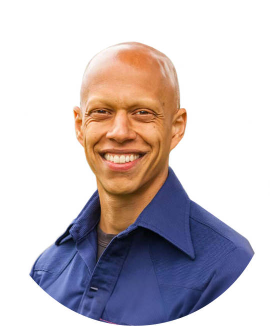 Smiling person with a shaved head, wearing a blue collared shirt, against a white background.