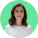 A woman with shoulder-length brown hair wearing a white top is facing the camera and smiling slightly. The background is a solid green circle.
