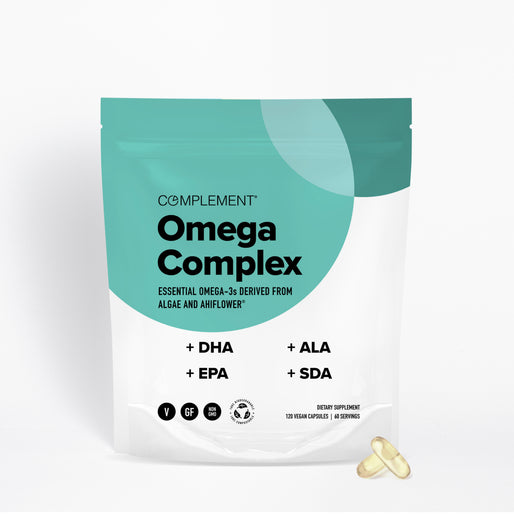 A teal and white pouch labeled Complement Omega Complex with text listing DHA, EPA, ALA, and SDA. The package states it contains vegan capsules. Two yellowish capsules are placed beside the pouch.