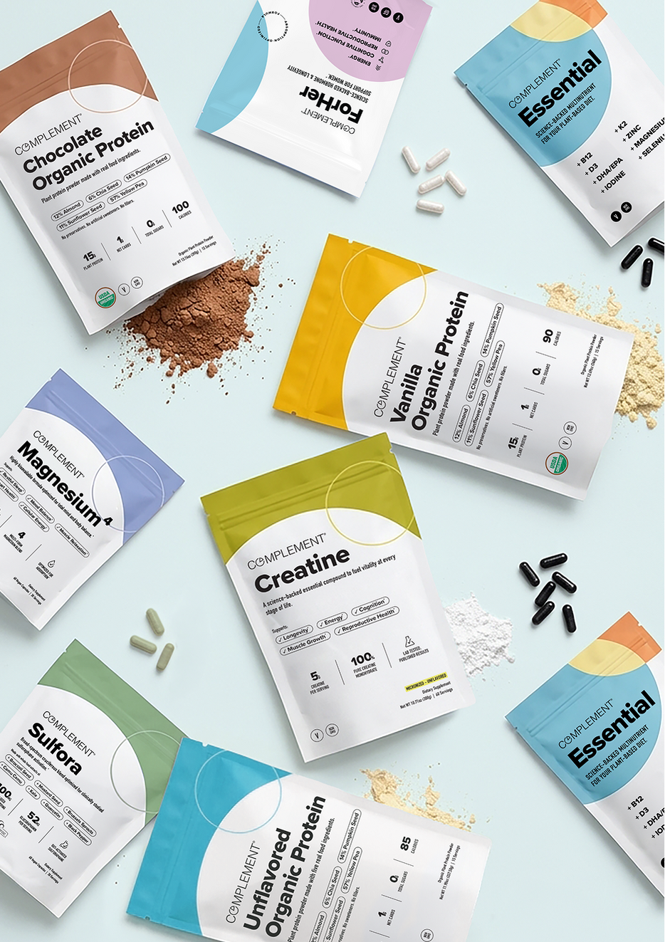 Various Complement supplement packets, including protein powders and capsules, are arranged on a light background with some powder and capsules scattered around the products.