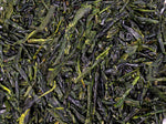 Close-up of loose-leaf green tea, showing dark green, twisted, and slightly glossy tea leaves tightly packed together.