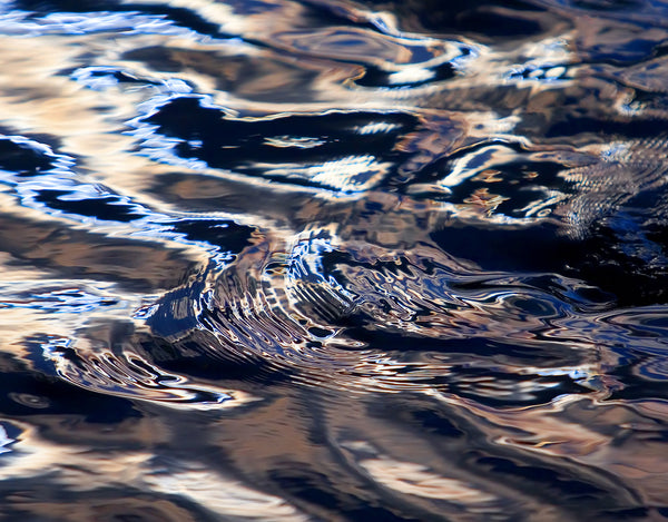Rippling water surface reflecting light, creating abstract patterns in shades of blue, white, and beige. The image has a wavy and fluid appearance.