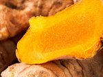 A close-up of a fresh turmeric root, showing its bright orange-yellow interior and textured brown skin.