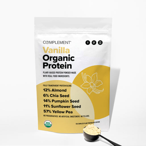 A bag of Complement Vanilla Organic Protein powder stands upright next to a scoop of the powder. The packaging lists ingredients: almond, chia seed, pumpkin seed, sunflower seed, and yellow pea.