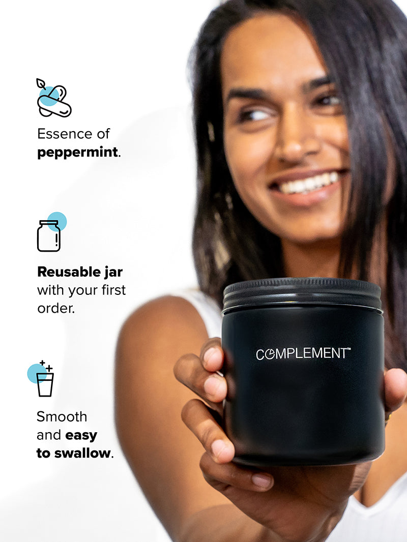 Woman holding matte black glass jar that stores Complement Essential vegan multivitamins with text that reads Essence of Peppermint, Reusable Glass Jar, Smooth and Easy to Swallow. 