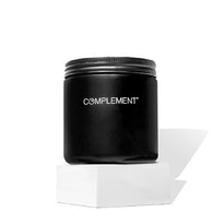 A black jar with the word COMPLEMENT on it sits atop a white hexagonal platform against a white background. The jar has a black screw-on lid.