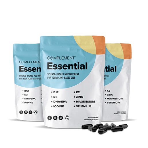Three bags of Complement Essential multinutrient supplements are shown. The bags display key ingredients, including B12, D3, DHA/EPA, iodine, K2, zinc, magnesium, and selenium. Black capsules are scattered in front.